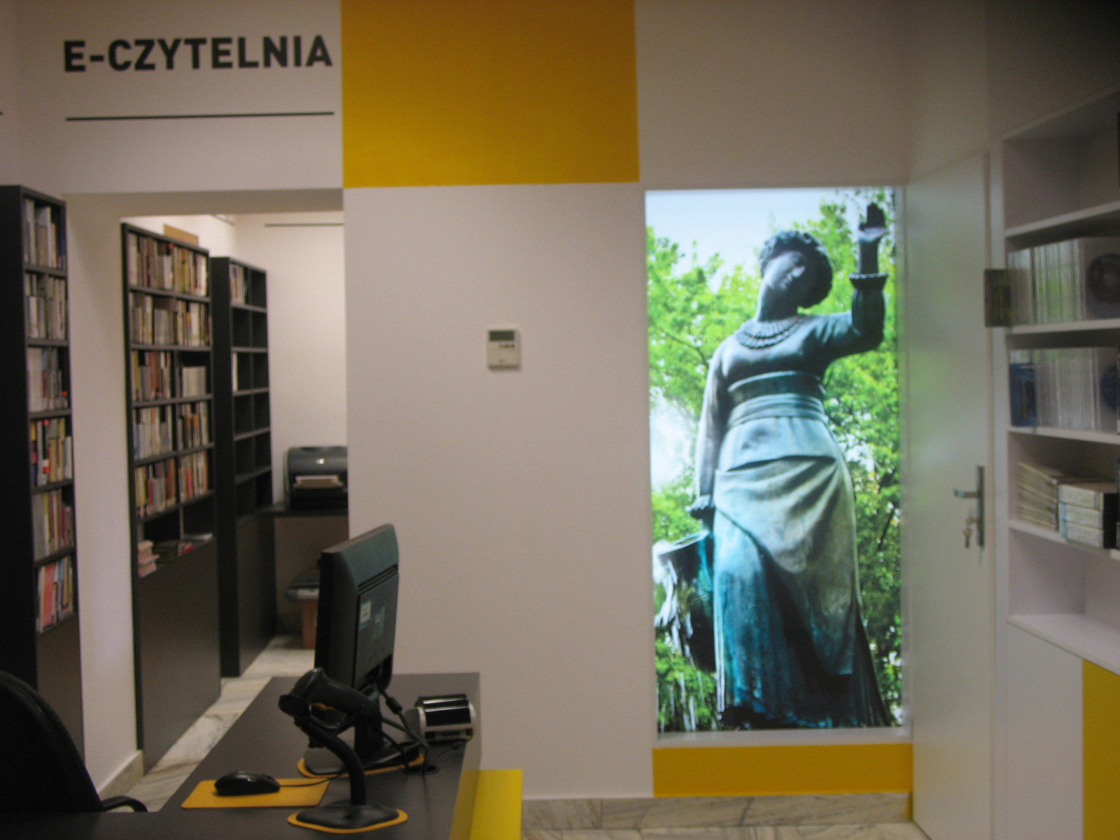 Czytelnia Naukowa nr 16 widok w środku na wejście do sali komputerowej oraz na duże zdjęcie pomnika "Dziewczyna z Dzbanem" (żoliborska Alina)