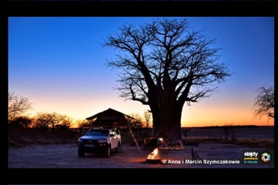 Samochód terenowy stoi przy olbrzymim baobabie. Na pierwszym planie płonie ognisko.