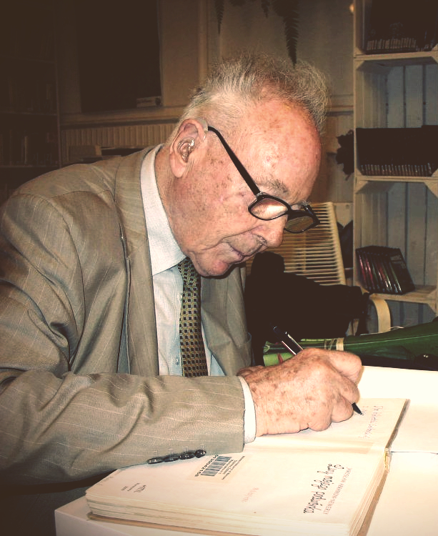 zdjęcie przedstawiające jarosława abramowa-newerlyego podpisującego książki z biblioteki żoliborskiej w czytelni pod sowami