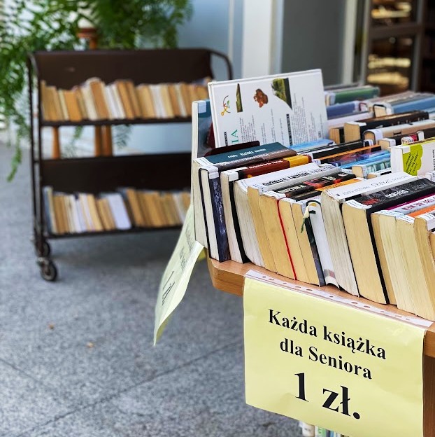 zdjęcie przedstawiające wystawę książek używanych na stole na dole napis na kartce każda książka dla seniora 1 zł.