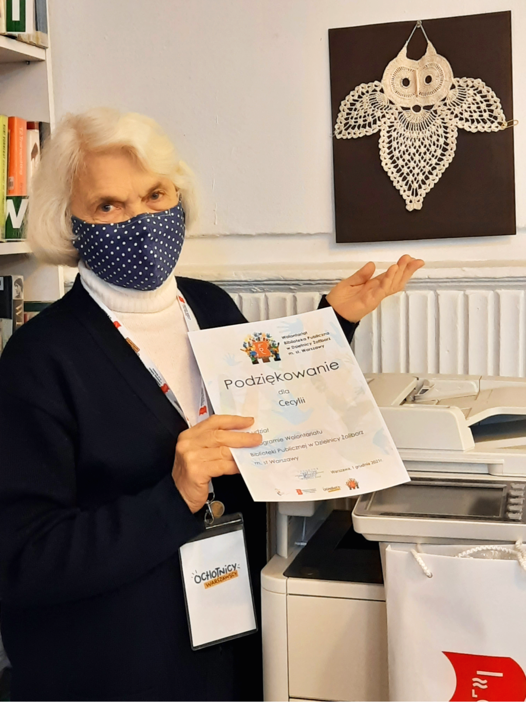 zdjęcie przedstawiające wolontariuszkę roku w czytelni naukowej w bibliotece publicznej w dzielnicy żoliborz m. st. warszawy. na dyplomie napis podziękowanie dla cecylii, na identyfikatorze napis ochotnicy warszawy