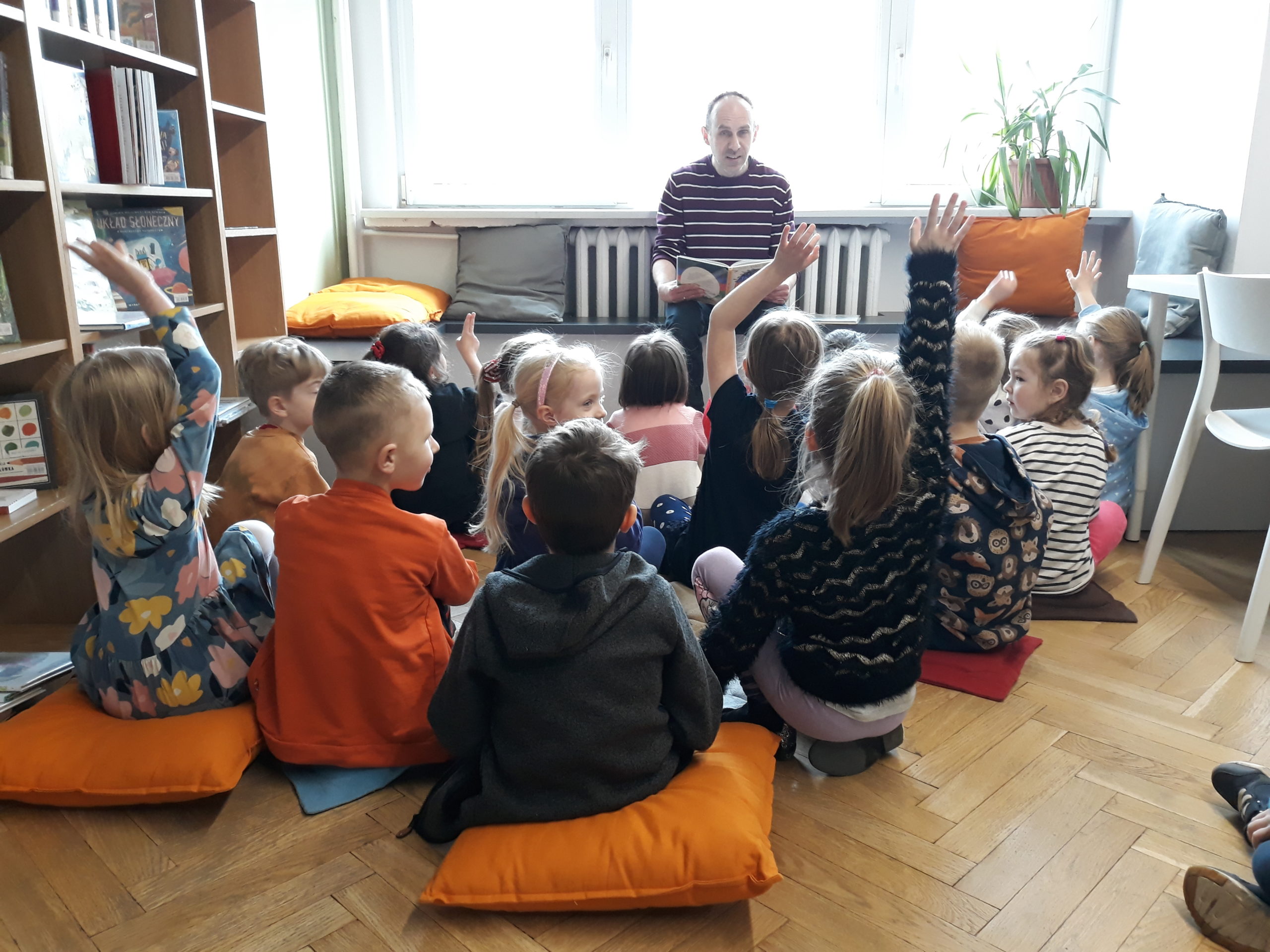 grafika wyróżniająca - przedstawiająca dzieci biorące udział w lekcji bibliotecznej , w bibliotece przy ul. Broniewskiego 9a