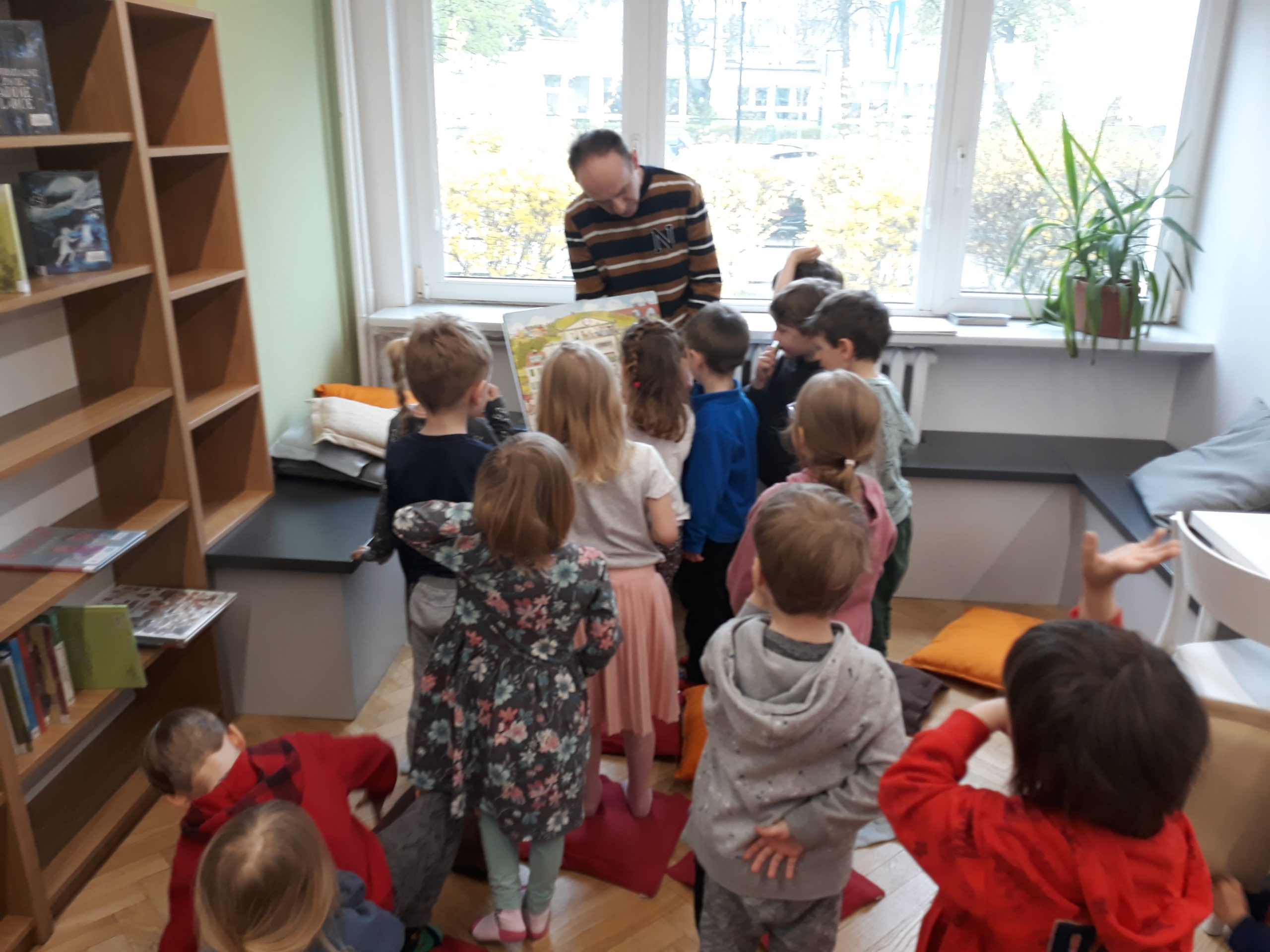 grafika wyróżniająca - przedstawiająca dzieci biorące udział w lekcji bibliotecznej , w bibliotece przy ul. Broniewskiego 9a