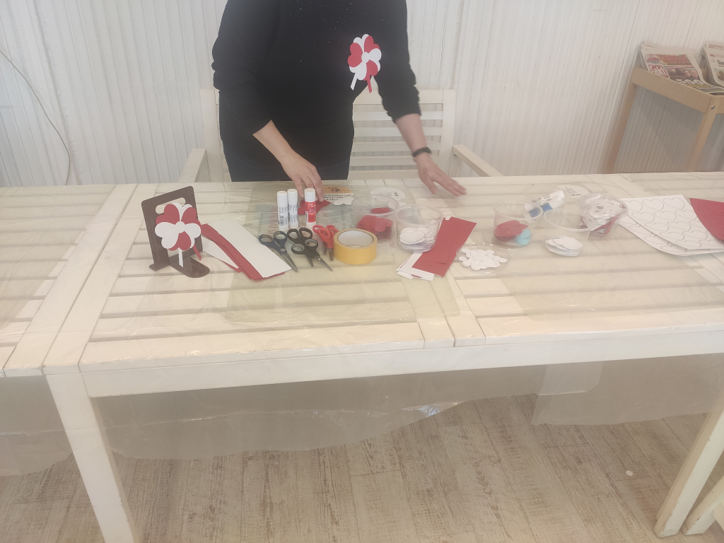 Uczestniczka warsztatów podczas tworzenia przypinki. Na stole rozłożone nożyczki, klej i kolorowy papier