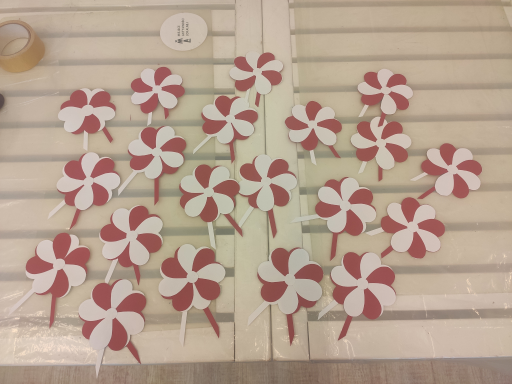 Na stole rozłożone przypinki w kształcie kwiatu w kolorach biało-czerwonych