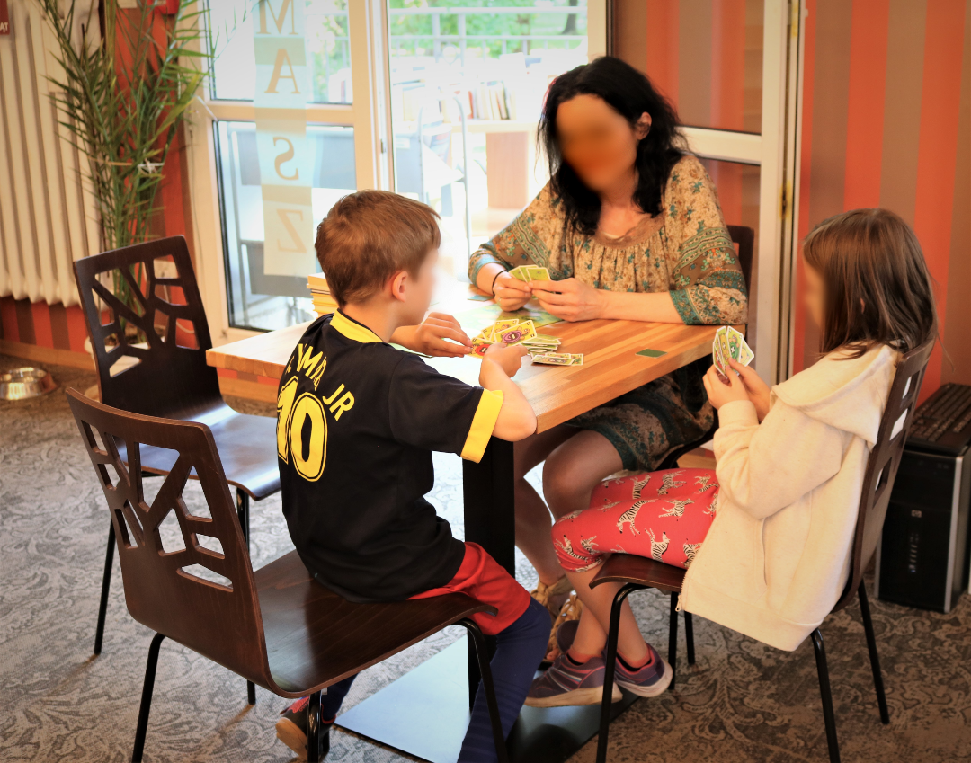 zdjęcie z planszówek zorganizowanych w wypożyczalni nr 16 podczas 19 ogólnopolskiego tygodnia bibliotek 2022, na pierwszym planie rodzina grająca w grę we wnętrzu biblioteki