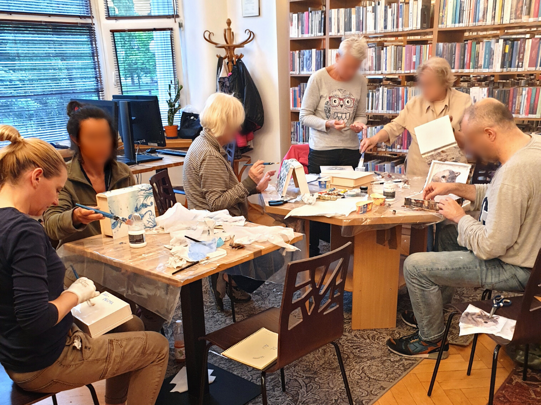 zdjęcie przedstawiające uczestników warsztatów z ozdabiania pudełek w kształcie książek metodądecoupage podczas naklejania wzorów i malowania pudełek białą farbą