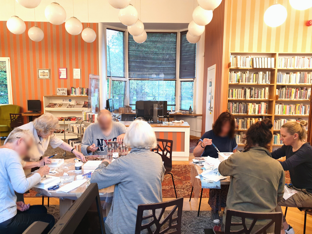zdjęcie przedstawiające uczestników warsztatów z ozdabiania pudełek w kształcie książek metodądecoupage podczas naklejania wzorów i malowania pudełek białą farbą