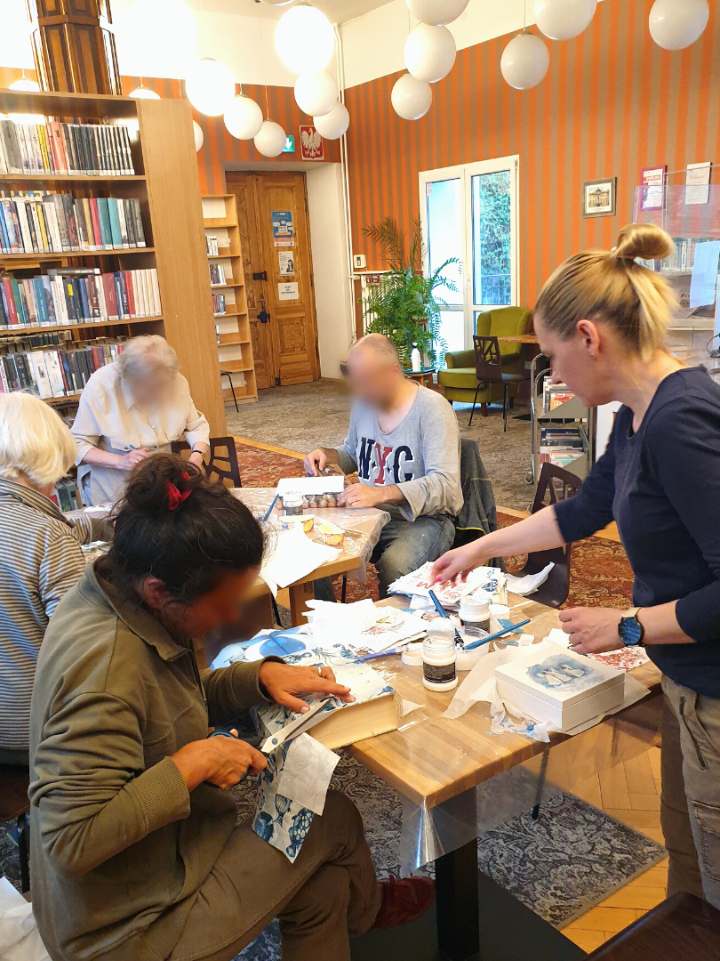 zdjęcie przedstawiające uczestników warsztatów z ozdabiania pudełek w kształcie książek metodą decoupage podczas naklejania wzorów