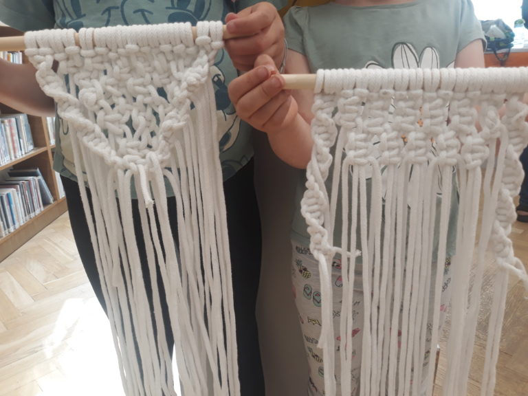 zdjęcie przedstawiające dwie uczestniczki warsztatów, które trzymają wykonane przez siebie makramy