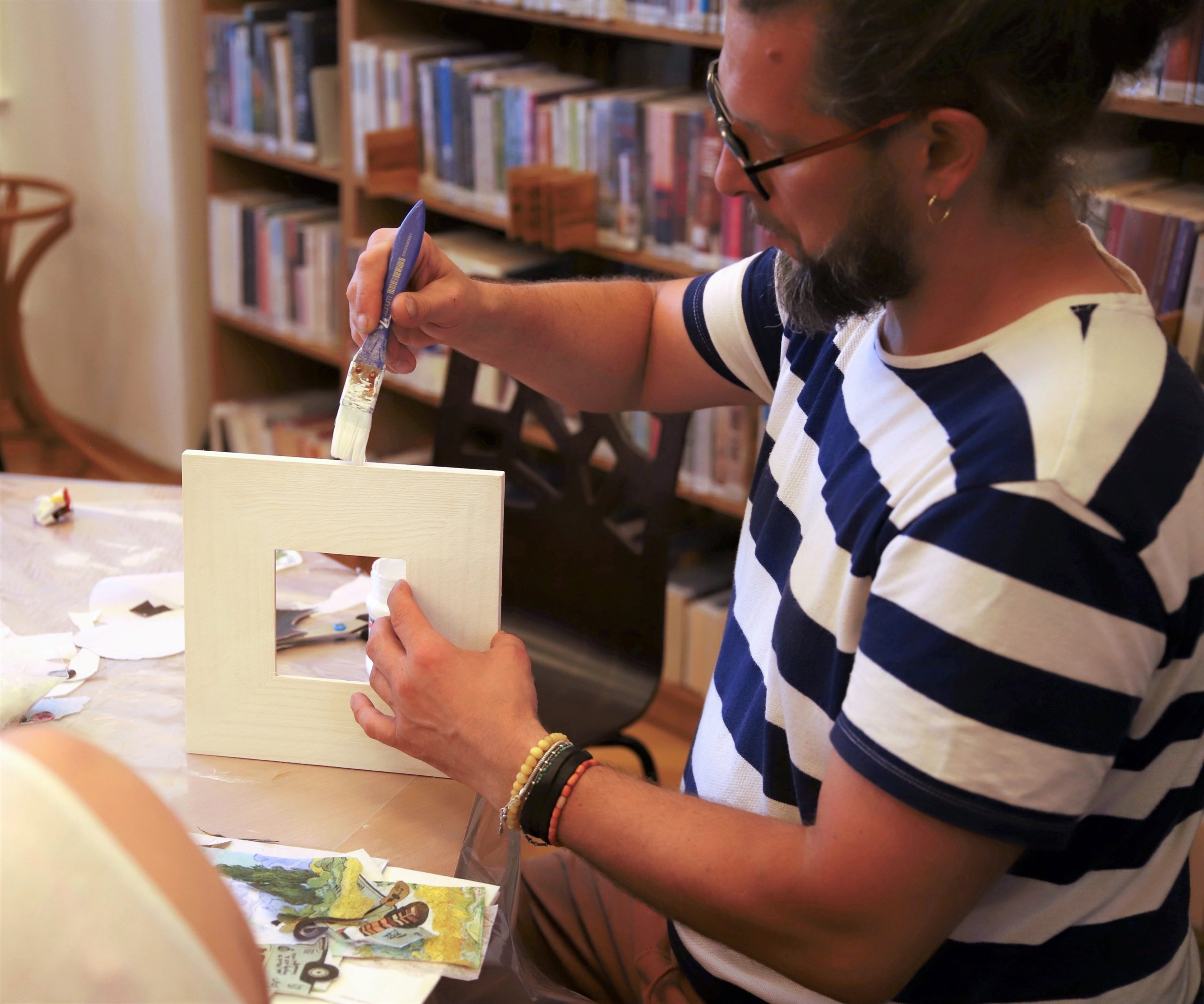 zdjęcie przedstawiające uczestnika warsztatów z ozdabiania ramek na zdjęcia metodą decoupage podczas malowania białą farbą