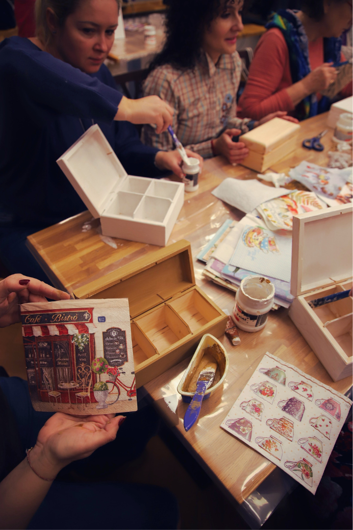 zdjęcie przedstawiające uczestników warsztatów z ozdabiania drewnianych herbaciarek metodą decoupage podczas malowania białą farbą, naklejania wzorów i wycinania wzorów we wnętrzu wypożyczalni nr 16