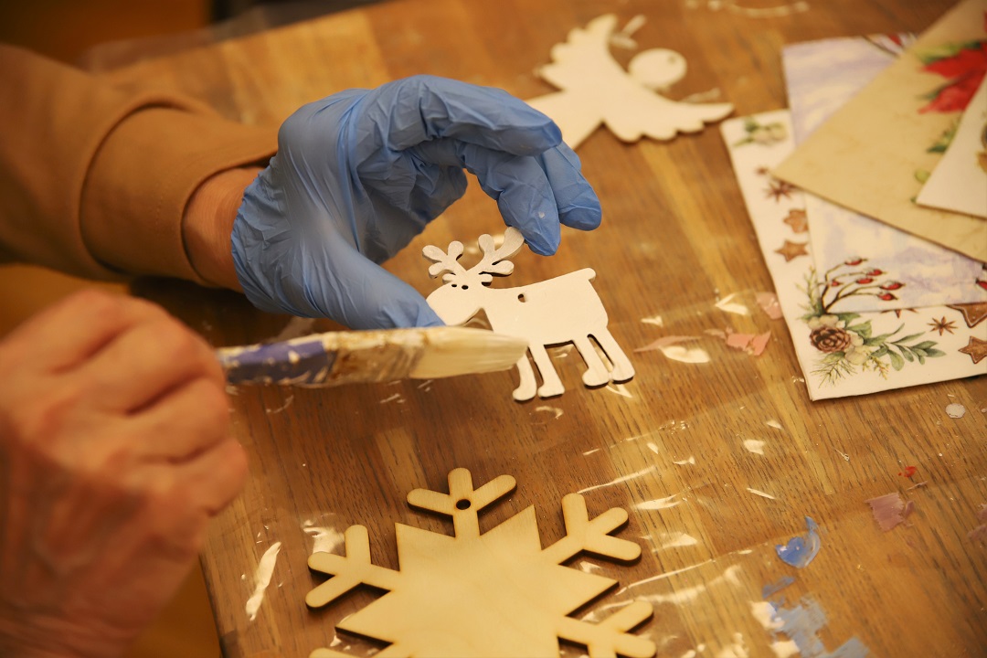 zdjęcie przedstawiające uczestnika warsztatów z ozdabiania drewnianych ozdób świątecznych metodą decoupage podczas malowania we wnętrzu wypożyczalni nr 16
