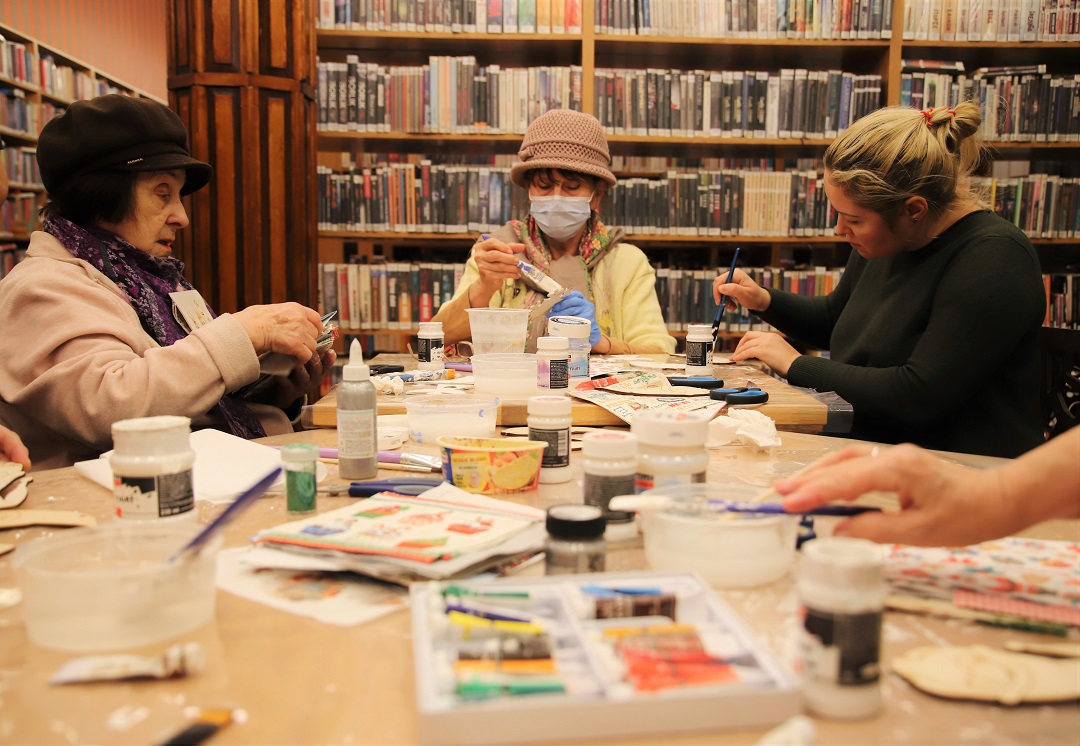 zdjęcie przedstawiające uczestników warsztatów z ozdabiania drewnianych ozdób świątecznych metodą decoupage podczas malowania białą farbą, naklejania wzorów i wycinania wzorów we wnętrzu wypożyczalni nr 16