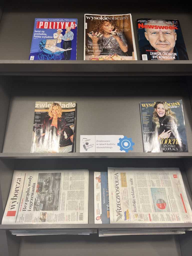 regał z gazetami, widoczne logo budżetu obywatelskiego