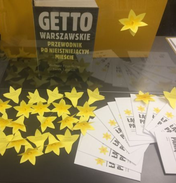 Na zdjęciu książka pt. "Getto Warszawskie: przewodnik po nieistniejącym mieście" oraz papierowe żółte żonkile i ulotki przypominające o powstaniu w getcie warszawskim