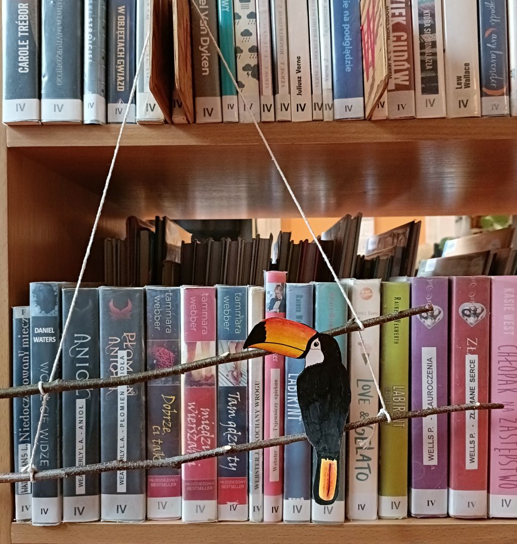 Praca uczestnika warsztatów artystycznych "Nasze ptaki". Uczestnik stworzył dekorację do powieszenia np. w oknie czy na ścianie w pokoju. Ozdoba składa się z powiązanych sznurkiem gałązek, na których umieszczono papierowe ptaki.