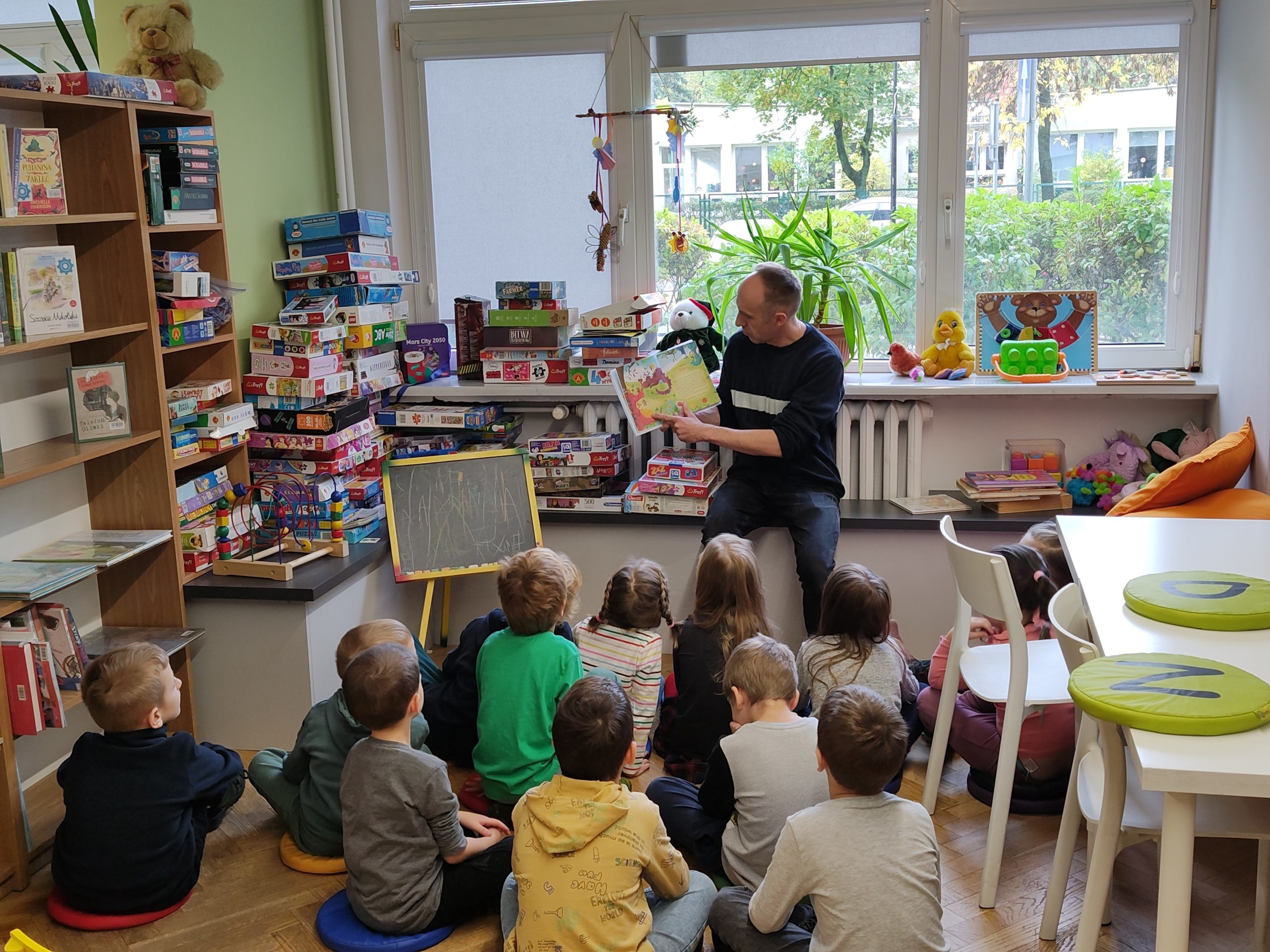 Dzieci słuchają z zaciekawieniem jednego z opowiadań czytanego przez bibliotekarza.