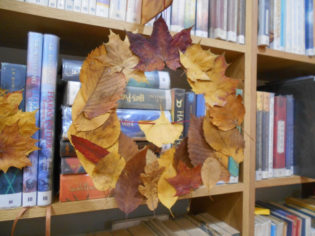 Wiszący na tle książek wieniec jesienny zrobiony z kolorowych jesiennych.