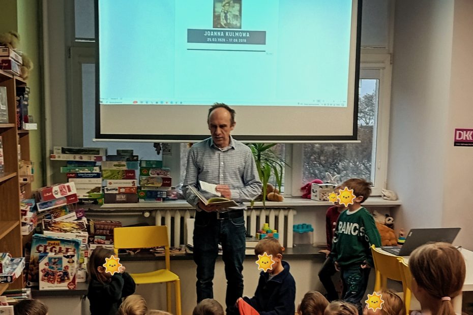 grafika wyróżniająca przedstawiająca bibliotekarza na tle ekranu, na którym widnieje portret Joanny Kulmowej. Przedstawia grupie dzieci jaki jest temat spotkania.