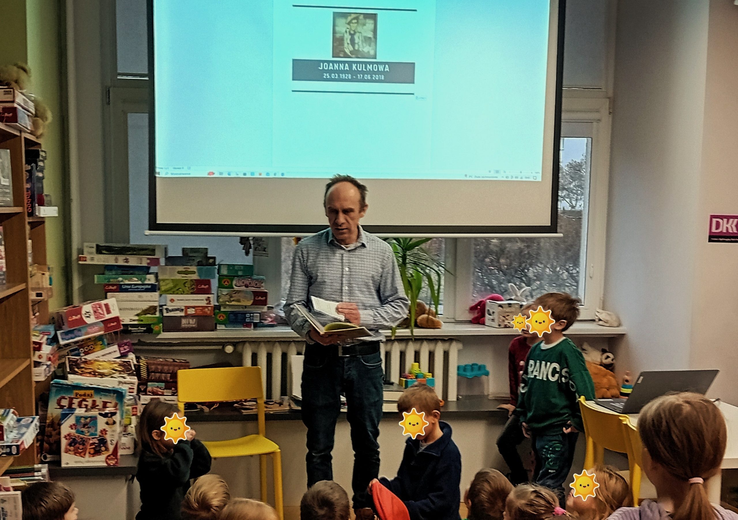 grafika wyróżniająca przedstawiająca bibliotekarza na tle ekranu, na którym widnieje portret Joanny Kulmowej. Przedstawia grupie dzieci jaki jest temat spotkania.