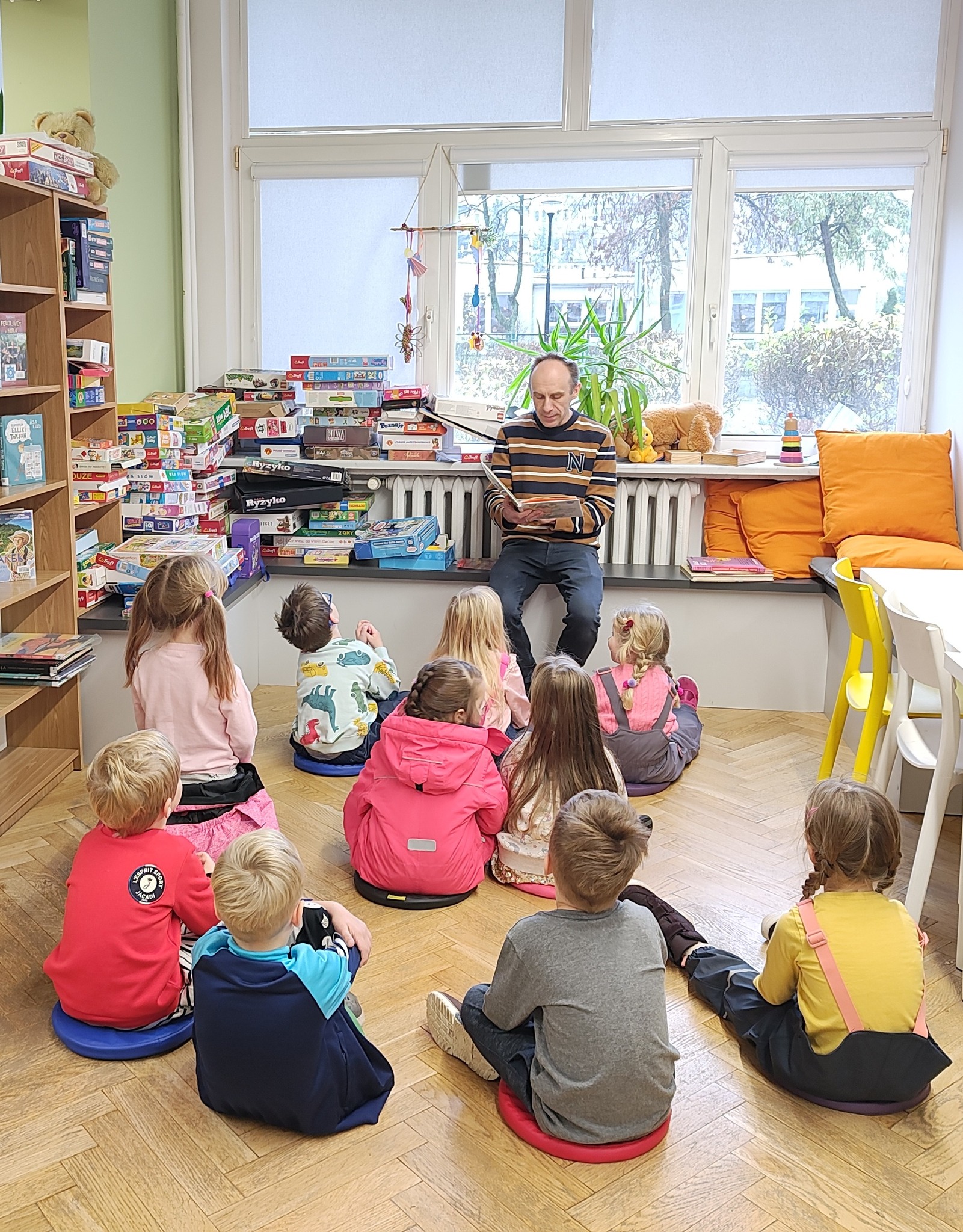 grafika wyróżniająca przedstawiająca bibliotekarza podczas czytania bajki grupie dzieciom.