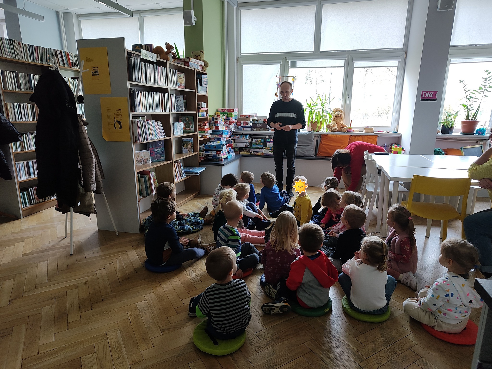 grafika wyróżniająca przedstawiająca bibliotekarza opowiadającego grupie dzieci o pracy w bibliotece.
