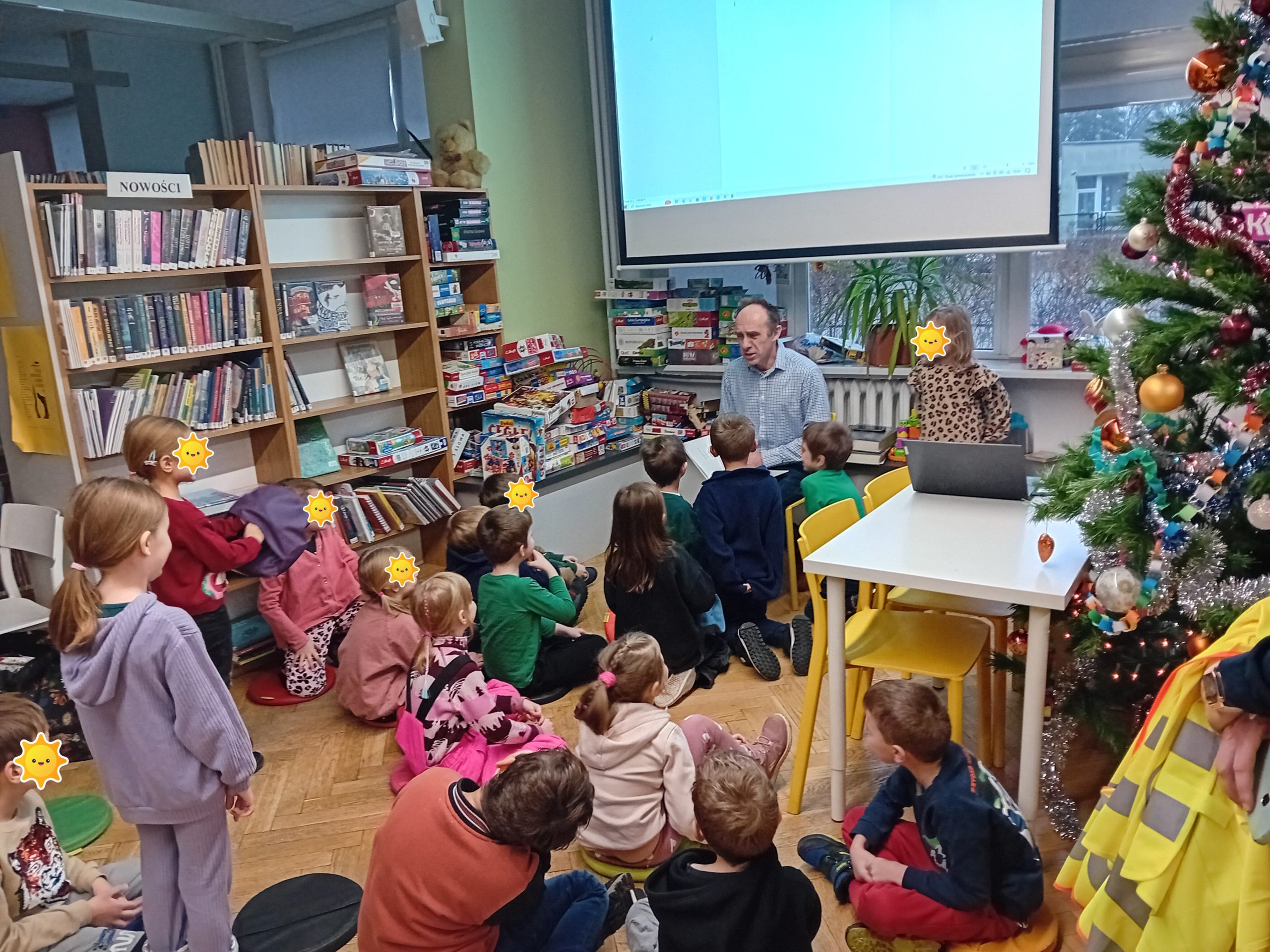 grafika wyróżniająca przedstawiająca bibliotekarza opowiadającego dzieciom o Joannie Kulmowej. Za bibliotekarzem znajduje się duży ekran. Na spotkaniu były czytane wiersze poetki.