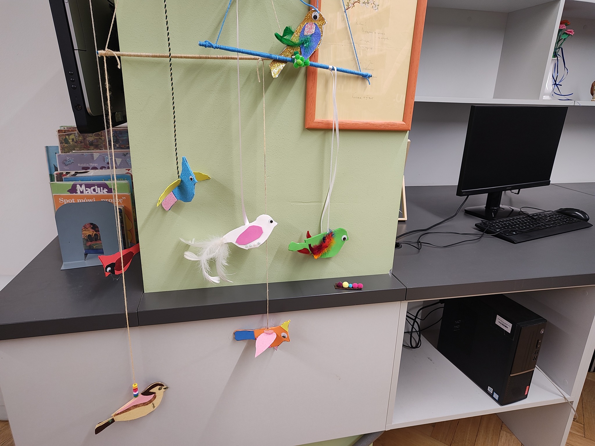 grafika wyróżniająca przedstawiająca wszystkie prace uczestników w jednym miejscu. Na patyczkach zawieszone są kolorowe ptaki wykonane z różnych materiałów plastycznych.