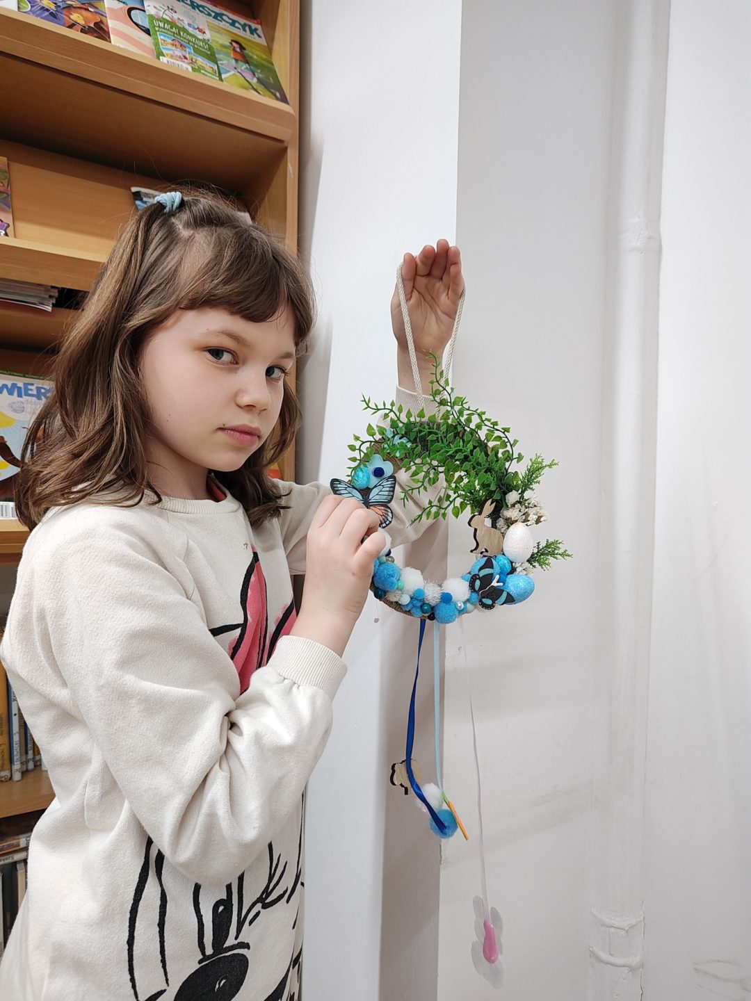 Dziewczynka prezentująca efekt swojej twórczej pracy. Ulubionym kolorem jest niebieski, który zdominował wielkanocną kompozycję uzupełnioną roślinnymi i drewnianymi elementami. Nie zabrakło też piórek i filcowych zająców.