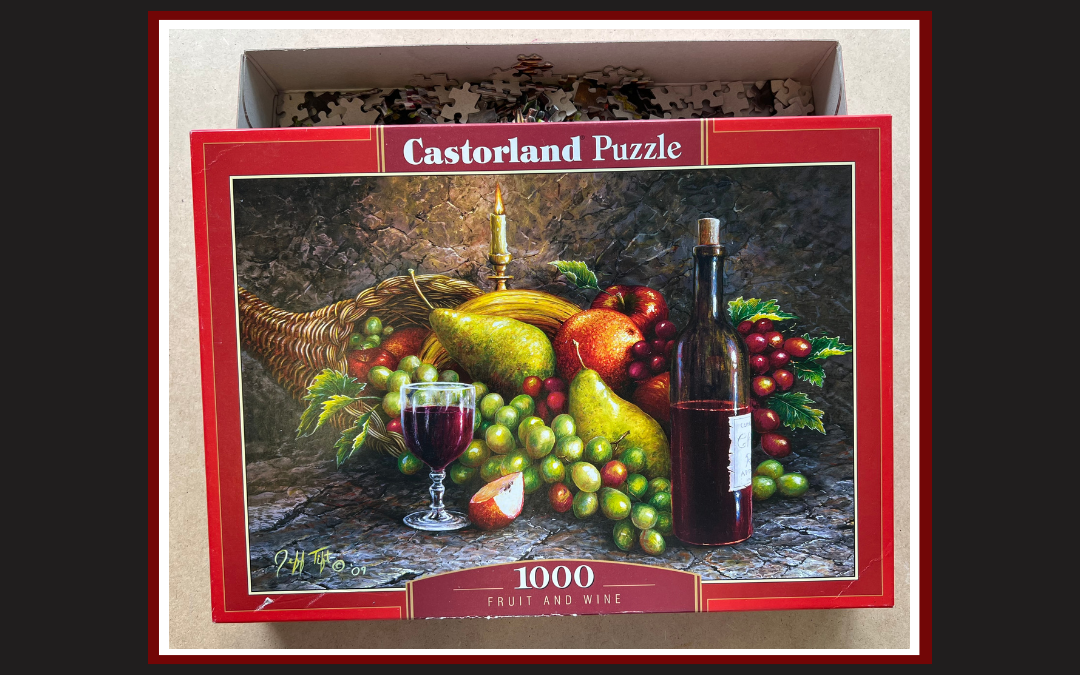 pudełko z puzzlami, na obrazku kompozycja z owoców i butelka wina