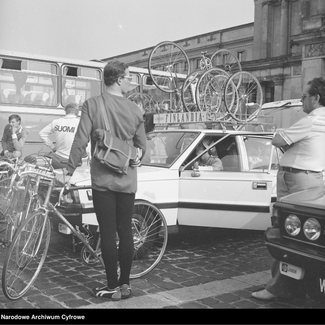 Fotografia z roku 1982, Grażyna Rutowska, Uczestnicy wyścigu przed gmachem Teatru Wielkiego. Widoczny m.in. samochód FSO Polonez z rowerami obsługujący kolarzy z Finlandii. Napis w dolnym lewym rogu: Narodowe Archiwum Cyfrowe.