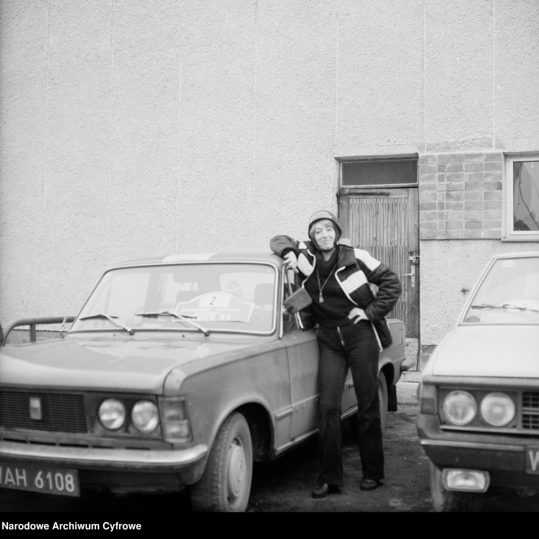 Fotografia z roku 1984, Grażyna Rutowska w kasku przy samochodzie Fiat 125 p. Obok samochód FSO Polonez. Napis w dolnym lewym rogu: Narodowe Archiwum Cyfrowe.