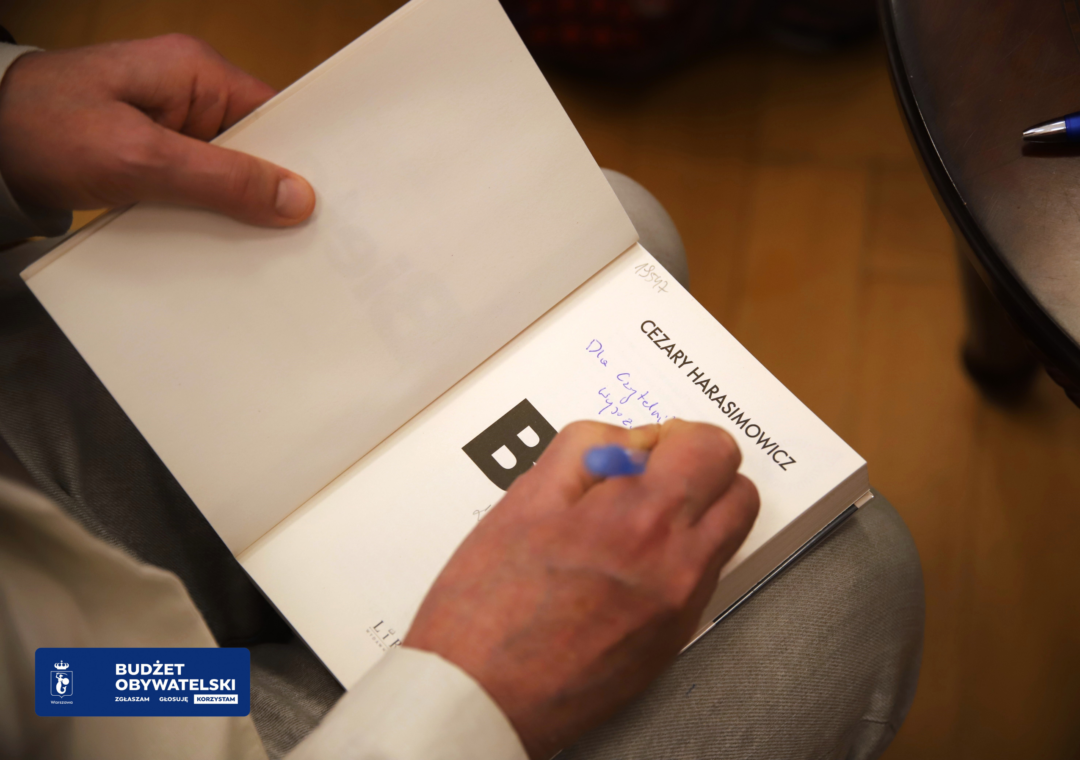 zdjęcie ze spotkania autorskiego z Cezarym Harasimowiczem oraz Elżbietą Ficowską 14 maja 2024 r. we wnętrzu Wypożyczalni nr 16. autor podpisuje książkę Bieta. w lewym dolnym rogu logo budżetu obywatelskiego: budżet obywatelski zgłaszam głosuję korzystam