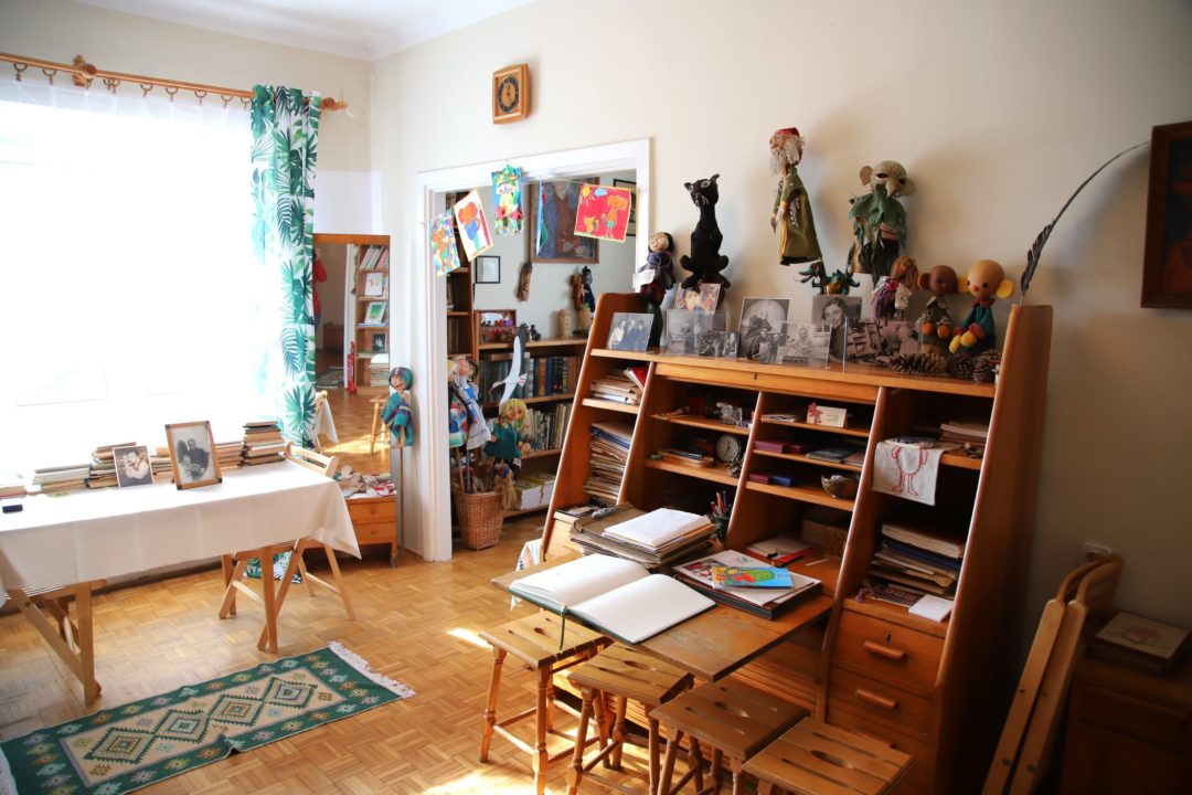 zdjęcie z wnętrza Muzeum Książki Dziecięcej lub inaczej Izby Pamięci Marii Kownackiej, która mieści się na warszawskim Żoliborzu przy ulicy Słowackiego 5/13 m. 74. zdjęcie pomieszczenia z biurkiem, regałami, stołem i różnymi przedmiotami.