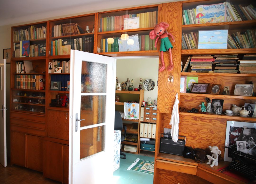 zdjęcie z wnętrza Muzeum Książki Dziecięcej lub inaczej Izby Pamięci Marii Kownackiej, która mieści się na warszawskim Żoliborzu przy ulicy Słowackiego 5/13 m. 74. zdjęcie pomieszczenia z regałami z książkami, wnęką na drzwi i widokiem na drugie pomieszczeniem