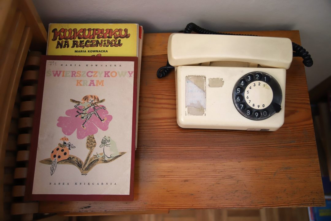 zdjęcie z wnętrza Muzeum Książki Dziecięcej lub inaczej Izby Pamięci Marii Kownackiej, która mieści się na warszawskim Żoliborzu przy ulicy Słowackiego 5/13 m. 74. zdjęcie przedmiotów na drewnianej szafie: książeczek kukuryku na ręczniku oraz świerszczykowy kram i starego aparatu telefonicznego