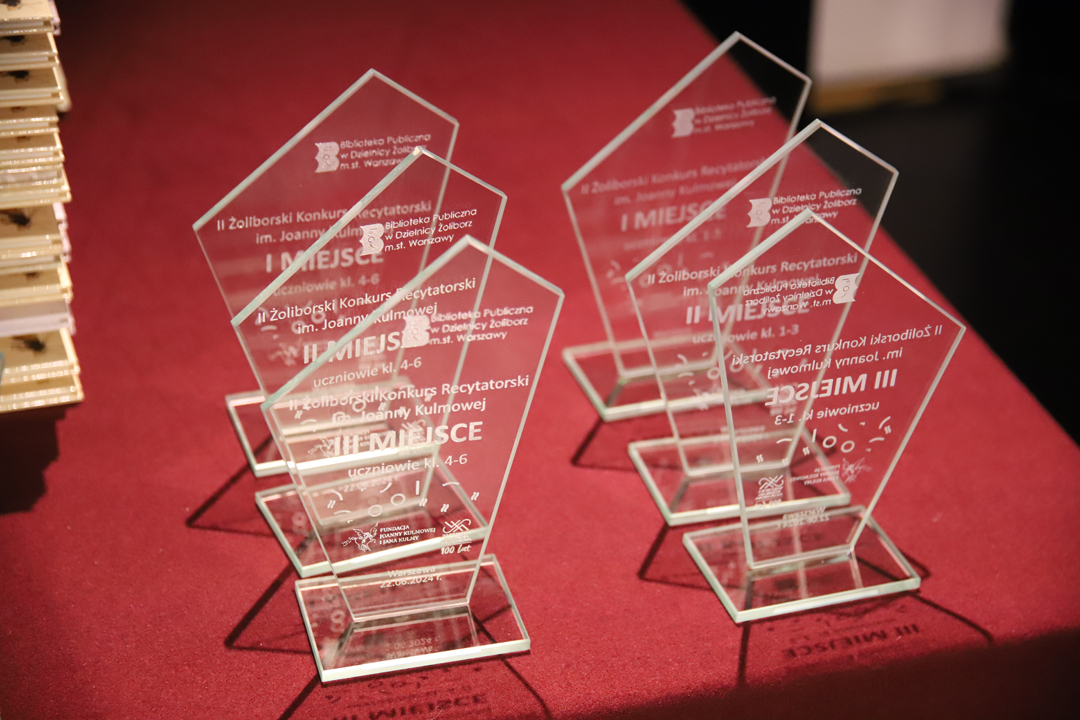 Zdjęcie z II Żoliborskiego Konkursu Recytatorskiego im. Joanny Kulmowej zorganizowanego przez Bibliotekę Publiczną w Dzielnicy Żoliborz, Społeczny Dom Kultury WSM oraz Fundację Joanny i Jana Kulmów. Przezroczyste tatuetki za pierwsze trzy miejsca z napisami: Biblioteka Publiczna w Dzielnicy Żoliborz m.st. Warszawy, II Żoliborski Konkurs Recytatoski im. Joanny Kulmowej, I, II lub III miejsce, uczniowie kl. 1-3, 4-6, 7-8. Fundacja Joanny Kulmowej i Jana Kulmy, WSM 100 lat.