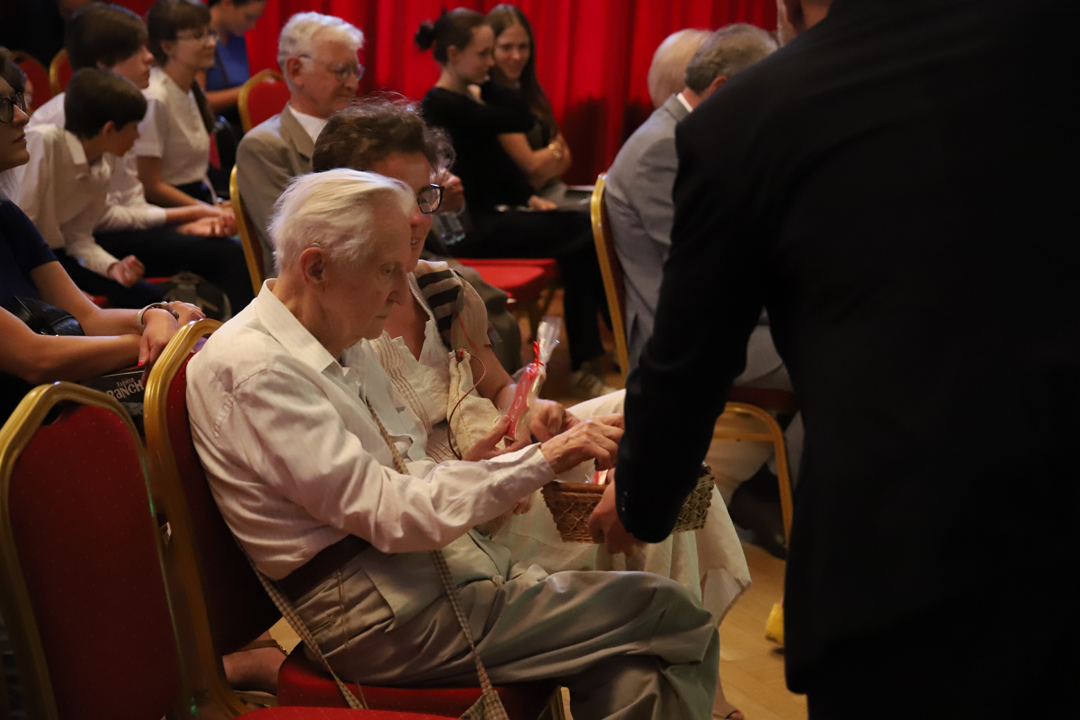 Zdjęcie z II Żoliborskiego Konkursu Recytatorskiego im. Joanny Kulmowej zorganizowanego przez Bibliotekę Publiczną w Dzielnicy Żoliborz, Społeczny Dom Kultury WSM oraz Fundację Joanny i Jana Kulmów. Widok na publiczność siedzącą przed sceną Społecznego Domu Kultury podczas rozdawania pamiątkowych ciasteczek z logiem Biblioteki.