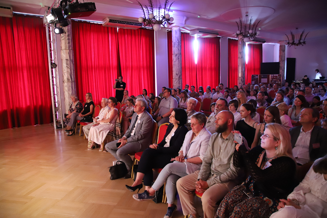 Zdjęcie z II Żoliborskiego Konkursu Recytatorskiego im. Joanny Kulmowej zorganizowanego przez Bibliotekę Publiczną w Dzielnicy Żoliborz, Społeczny Dom Kultury WSM oraz Fundację Joanny i Jana Kulmów. Widok na publiczność siedzącą przed sceną Społecznego Domu Kultury. W tle zasłonietę okna.