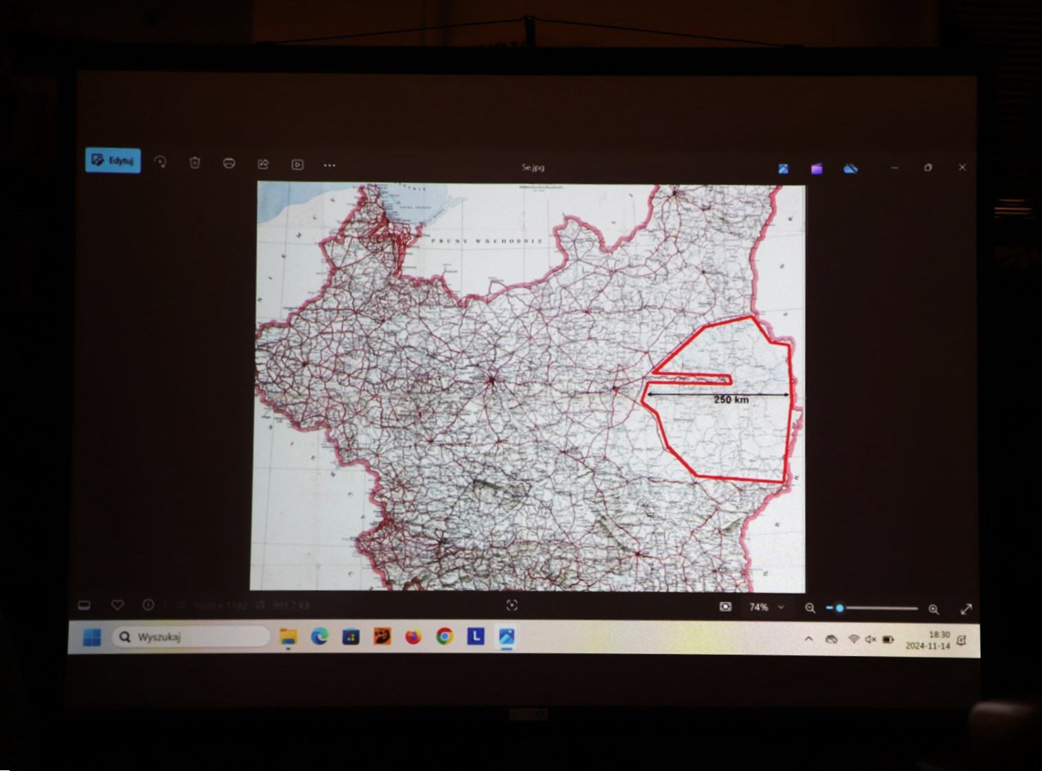 Zdjęcie z prelekcji "Motoryzacja Polska w Dwudziestoleciu Międzywojennym" we wnętrzu Wypożyczalni nr 16. Slajd z rzutnika z fragmentem mapy dróg przedwojennej Polski i zaznaczonym obszarem z napisem 250 km.