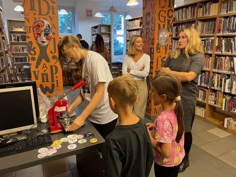 Nastoletnia wolontariuszka biblioteki przygotowuje dla dzieci i ich mam przypinki z okazji Nocy Bibliotek.