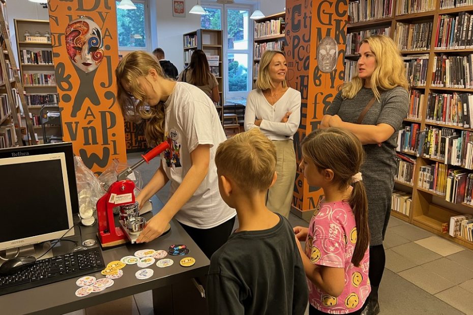 Nastoletnia wolontariuszka biblioteki przygotowuje dla dzieci i ich mam przypinki z okazji Nocy Bibliotek.