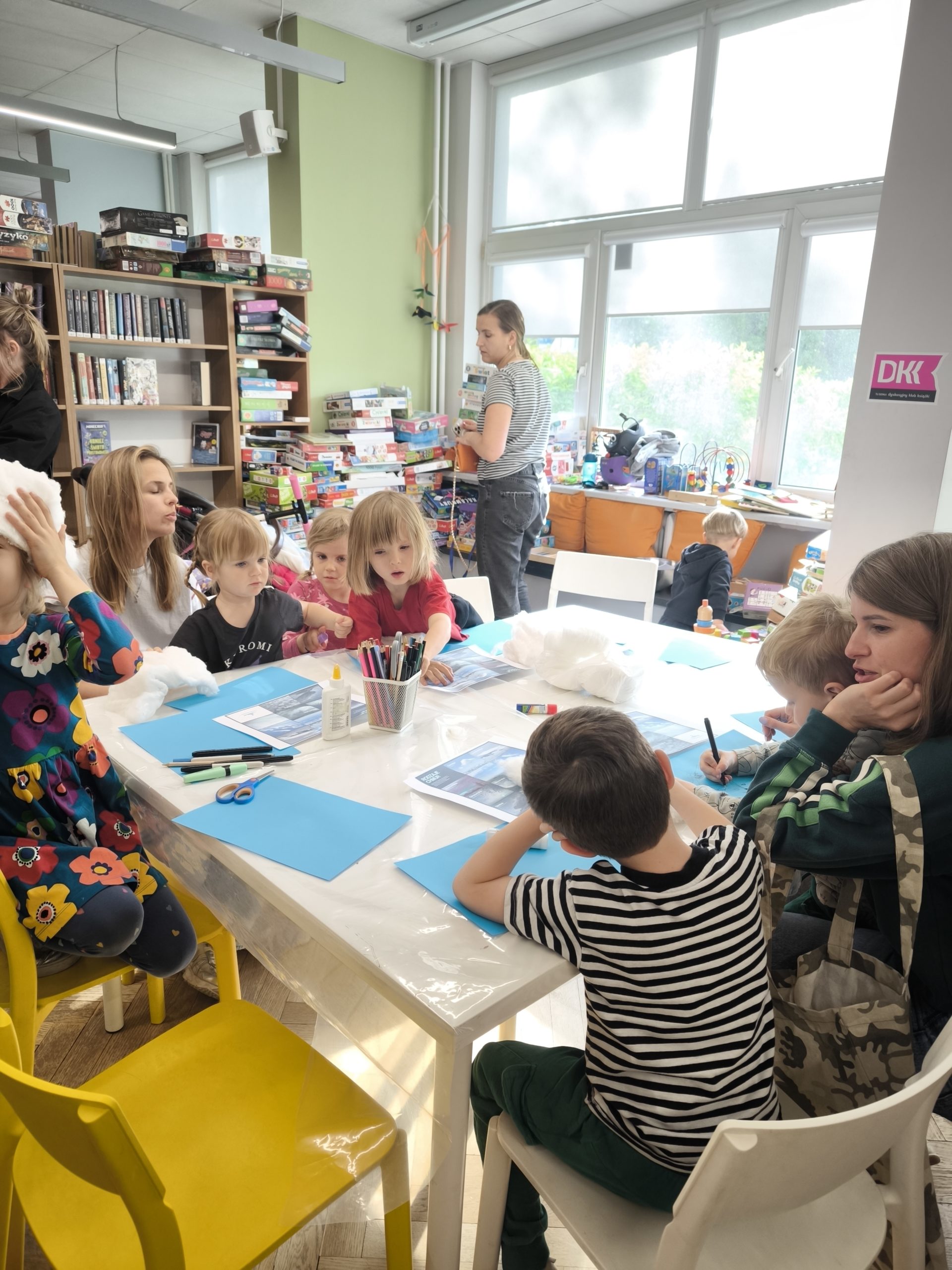 zdjecie z warsztatów "to nie magia, to nauka - wiosenne slajmy" we wnętrzu wypożyczalni nr 138 i biblioteki dla dzieci nr XV przy ul. Broniewskiego 9a. grupa dzieci, które wykonują eksperymenty przy stole
