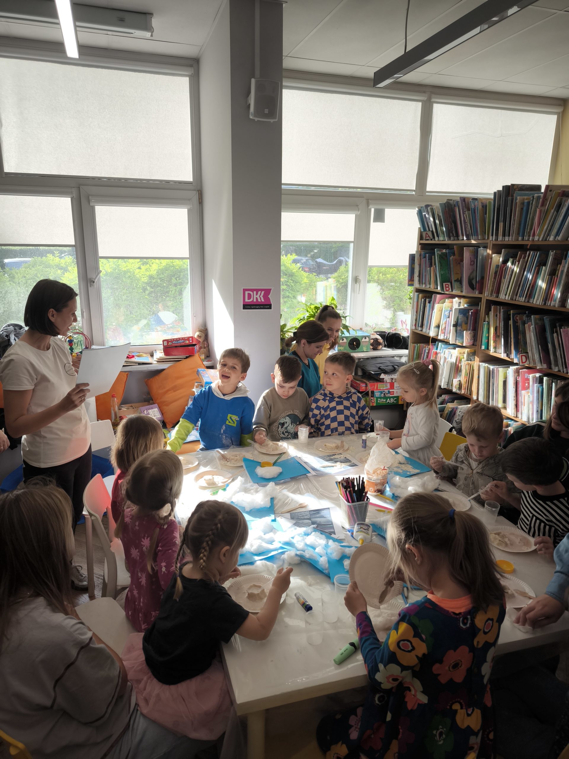 zdjecie z warsztatów "to nie magia, to nauka - wiosenne slajmy" we wnętrzu wypożyczalni nr 138 i biblioteki dla dzieci nr XV przy ul. Broniewskiego 9a. grupa dzieci, które wykonują eksperymenty przy stole