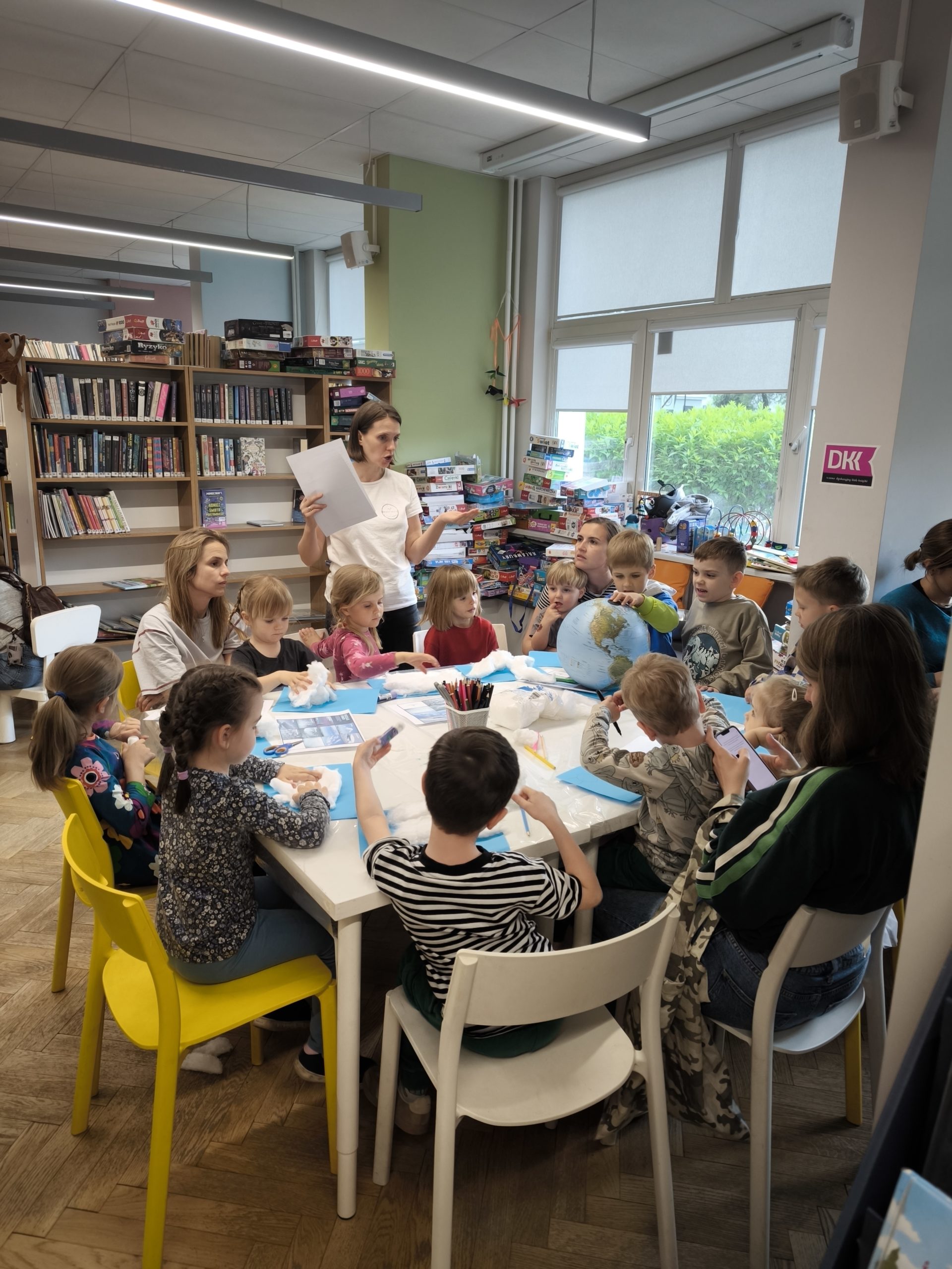 zdjecie z warsztatów "to nie magia, to nauka - wiosenne slajmy" we wnętrzu wypożyczalni nr 138 i biblioteki dla dzieci nr XV przy ul. Broniewskiego 9a. grupa dzieci, które wykonują eksperymenty przy stole