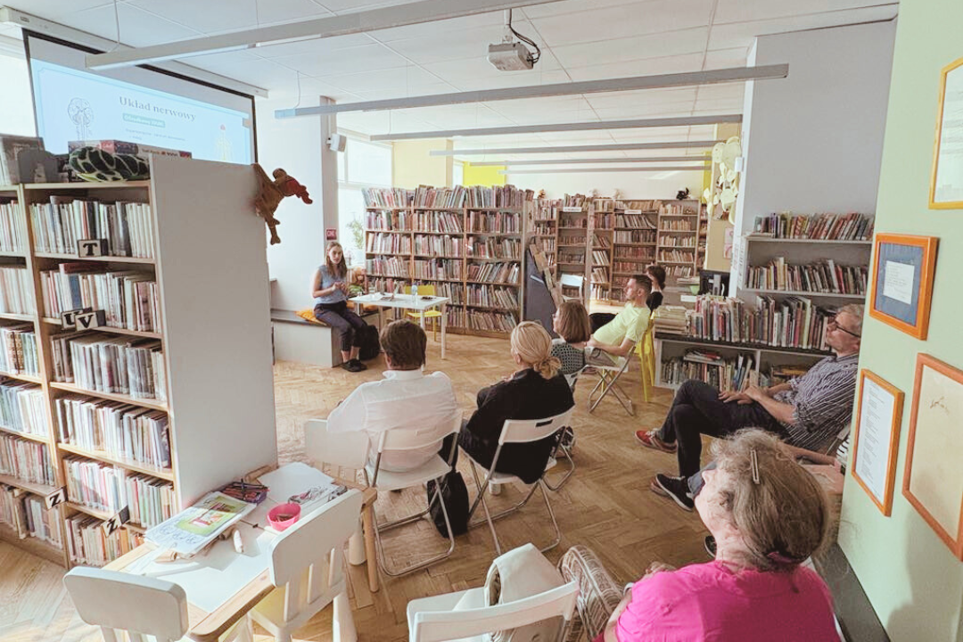 zdjecie osoby mówiącej do zgromadzonych we wnętrzu biblioteki dla dzieci nr xv słuchaczy na tle rzutnika ze slajdem.