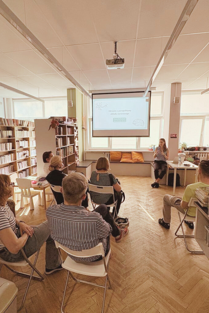 zdjecie osoby mówiącej do zgromadzonych we wnętrzu biblioteki dla dzieci nr xv słuchaczy na tle rzutnika ze slajdem.