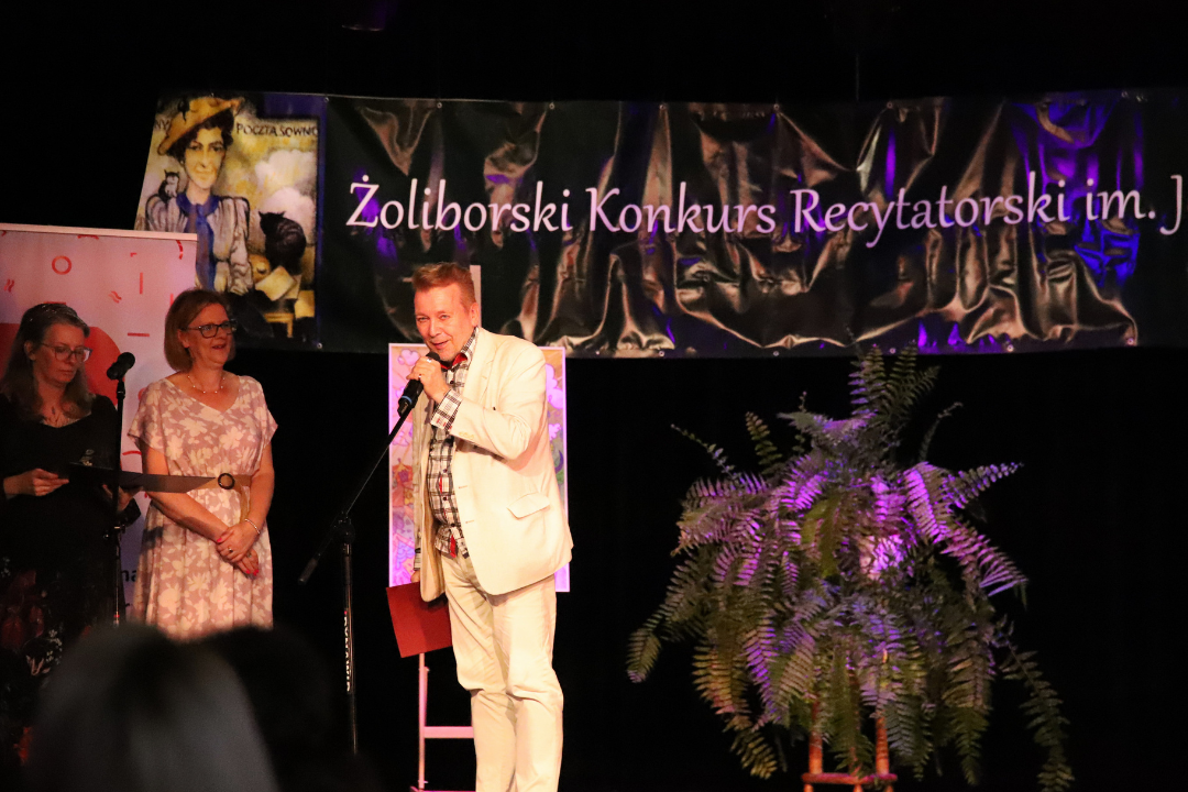 Zdjęcie z III Żoliborskiego Konkursu Recytatorskiego im. Joanny Kulmowej zorganizowanego przez Bibliotekę Publiczną w Dzielnicy Żoliborz, Społeczny Dom Kultury WSM oraz Fundację Joanny i Jana Kulmów. Dwie kobiety i mężczyźna stoją na scenie i mówią do mikrofonu.