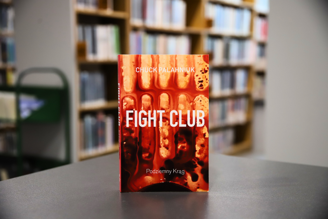 zdjecie przedstawia okładkę książki fight club Chucka palahniuka na tle wnętrza wypożyczalni nr 138, widoczne napisy:chuck palahniuk fight club podziemny krąg